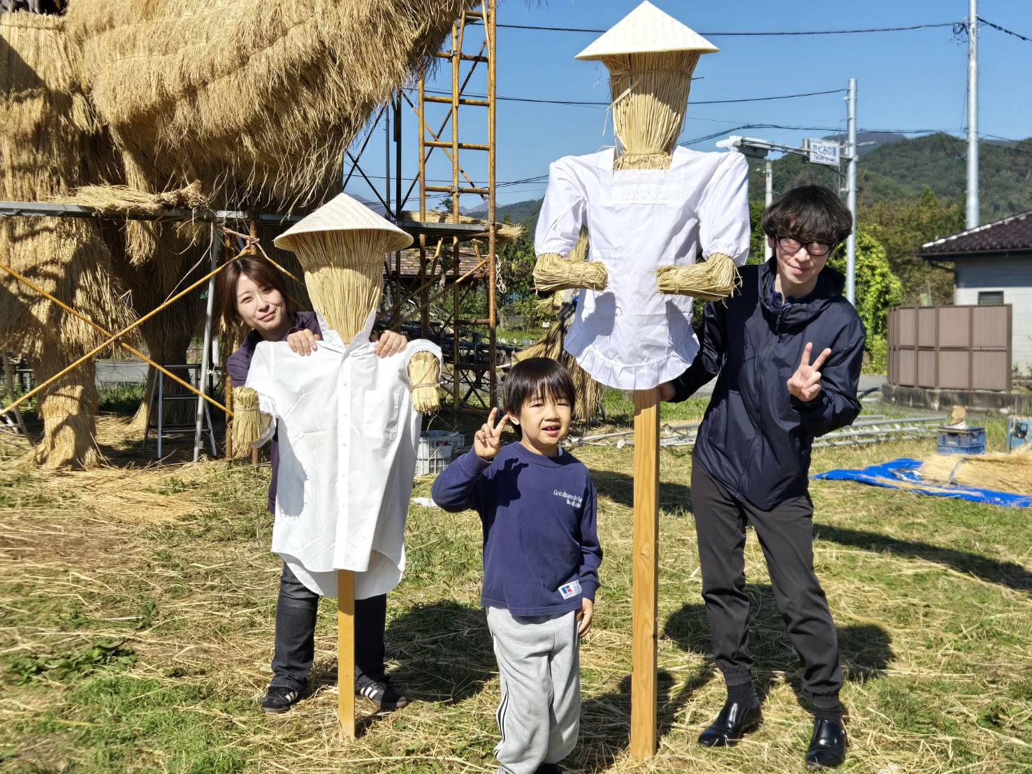 わらと白い服で作ったかかし2体を囲む、協働制作の参加者