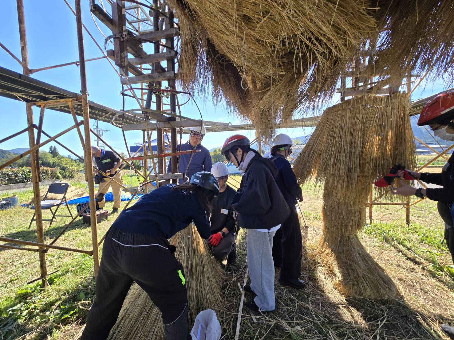 迷惑龍の足元で、わらの束を取り付ける協働制作の作業風景